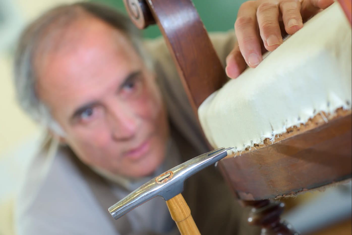Tapicero artesano restaurando un mueble con martillo en su taller de Madrid